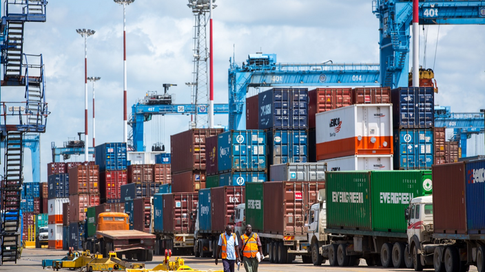 Two people walking beside a row of containers in harbor