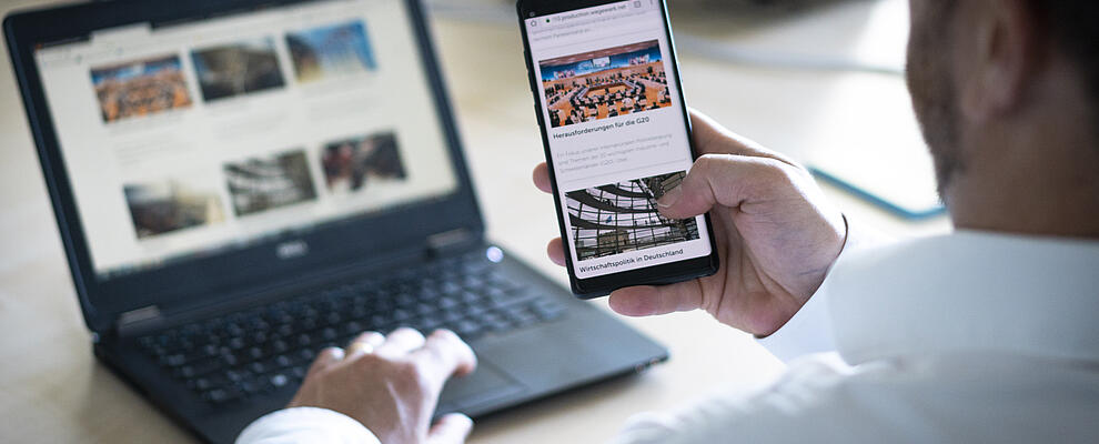 Person sitting in front of a laptop holding a mobile phone