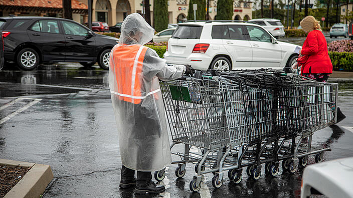 Essential worker at grocery store in rain coat collecting shopping carts in the rain