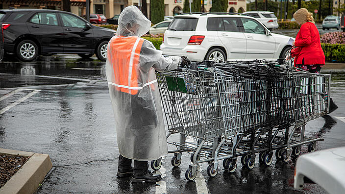 Essential worker at grocery store in rain coat collecting shopping carts in the rain