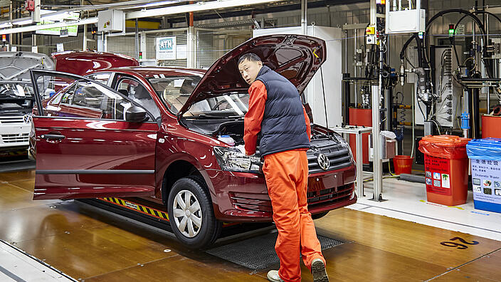 Arbeiter, der Autos auf der Montagelinie von Shanghai Volkswagen installiert / Worker who installs cars on the Shanghai Volkswagen factory assembly line