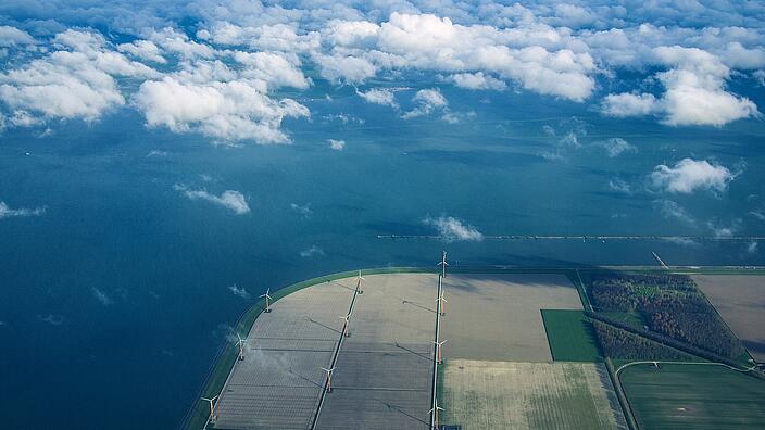 View from above onto the coast of the netherlands. Wind power stations in a field right behind the dike
