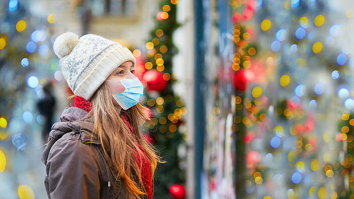 Mädchen trägt Gesichtsmaske auf einer Pariser Straße oder auf Weihnachtsmarkt / Girl wearing face mask on a Parisian street or at Christmas market looking at shop windows