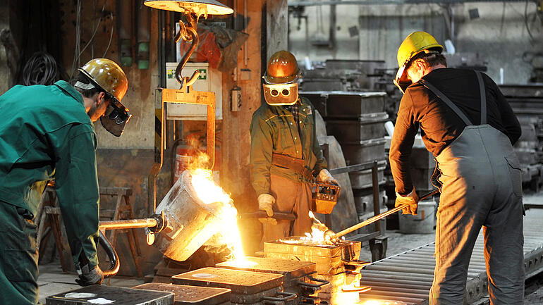 Gruppe von Arbeitern in einer Gießerei bei dem Schmelzofen / Group of workers in a foundry at the melting furnace