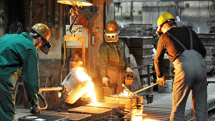 Gruppe von Arbeitern in einer Gießerei bei dem Schmelzofen / Group of workers in a foundry at the melting furnace