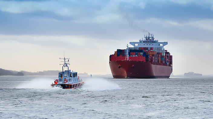 Ein kleines Lotsenboot vor einem riesigen Containerschiff auf dem Fluss Elbe, Deutschland / A small pilot boat in front of a huge container ship on the river Elbe, Germany