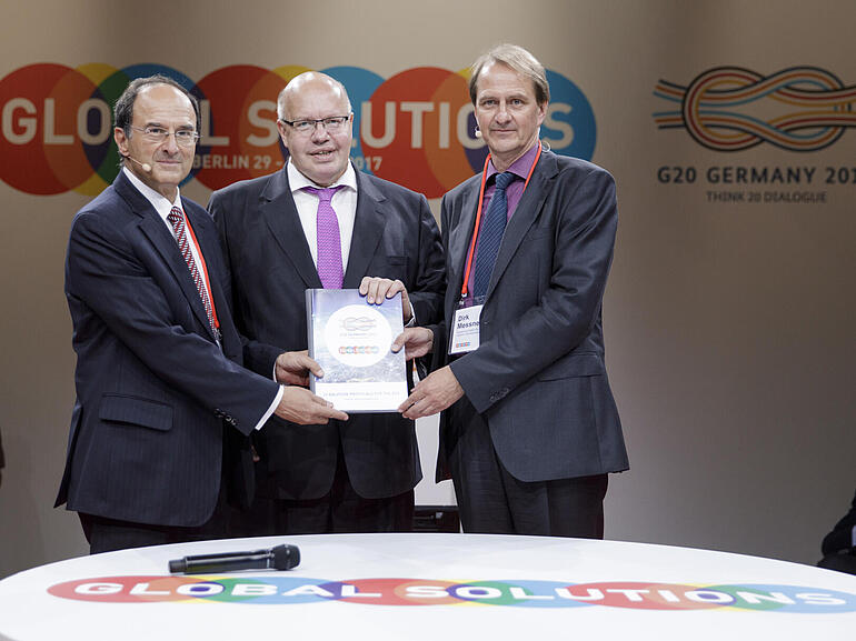 Dennis Snower (left) and Dirk Messner (right) hand over the brochure "20 Solutions for G20" to Peter Altmaier.