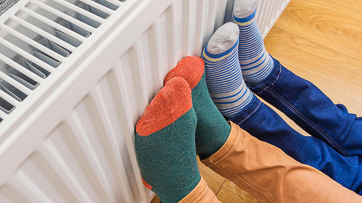 Woman and child wearing colorful pair of woolly socks warming cold feet in front of heating radiator
