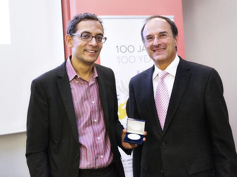 Abhijit Banerjee und Dennis Snower lächeln und zeigen die Medaille, die Banerjee bei der Bernhard Harms Preis Verleihung bekommen hat.