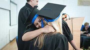 Two young women embrace to celebrate their graduation.