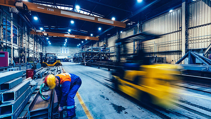 Factory work. Forklift moving and a worker taking a steel profile