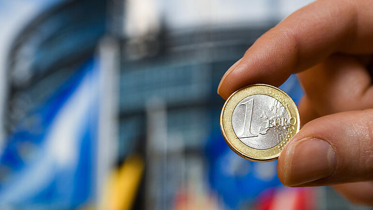 Person holding 1 Euro coin in front of EU Parliament