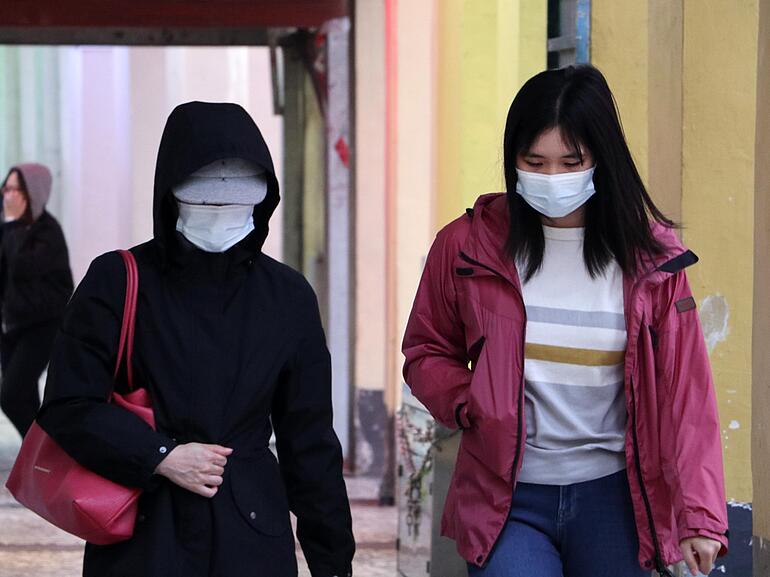 Two women walking in public wearing masks